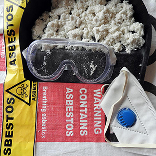 protective goggles and mask laying next to insallation and asbestos warning label