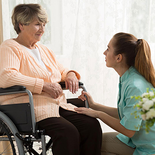 nurse kneeling and assisting elderly woman in wheelchair