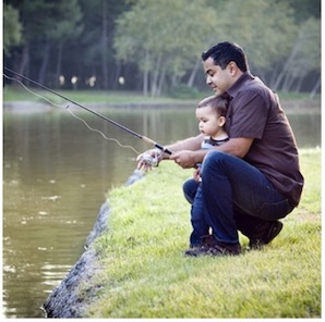 Man fishing with a child on the banks of a river.